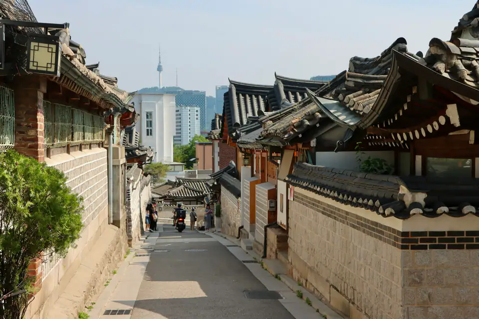 A narrow hanok lane with the modern city beyond — Bukchon Hanok Village, Seoul