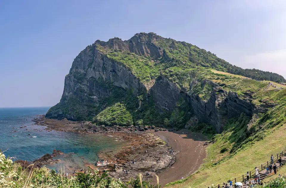 The green crater rising over the sea and rocky shore — Seongsan Ilchulbong, Jeju